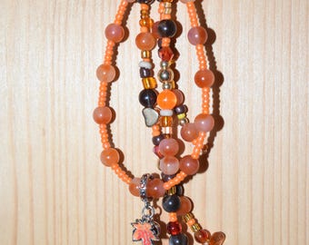 May include: A beaded keychain with orange, brown, and clear beads. The keychain has a silver charm with a red and orange leaf design and a decorative orange pumpkin bead. The beads are strung on a silver chain.
