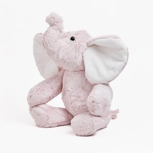 May include: A plush pink elephant toy with large white-lined ears and a raised trunk. The stuffed animal is sitting upright, with its legs extended. The elephant has a soft, textured appearance and a friendly expression.