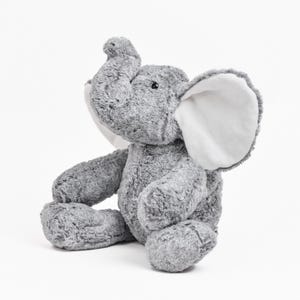 May include: A plush gray elephant toy with large, white-lined ears and a raised trunk. The stuffed animal is sitting with its legs extended and arms resting on its legs. The elephant has a soft, textured appearance.