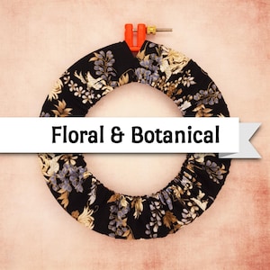 May include: A black embroidery hoop with floral fabric. The fabric features a pattern of white, gold, and purple flowers and leaves. The text "Floral & Botanical" is displayed on a white banner across the image.