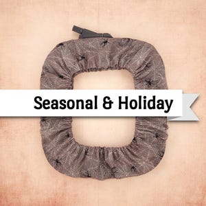 May include: A gray Halloween-themed cover with a spiderweb and spider pattern. The cover has a black handle and the text "Seasonal & Holiday" on a white banner.