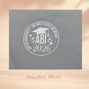 K&ouml;nnte beinhalten: Eine graue Abschlusskarte mit einem wei&szlig;en kreisf&ouml;rmigen Design. Das Design enth&auml;lt eine Abschlusskappe, das Wort "ABI" und das Jahr "2026". Der Text "DIE WELT STEHT DIR OFFEN!" ist ebenfalls enthalten.