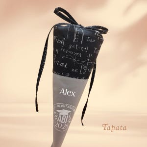 K&ouml;nnte beinhalten: Eine Geschenkt&uuml;te zur Abschlussfeier mit einem schwarzen Oberteil, das mit wei&szlig;en mathematischen Gleichungen gemustert ist, und einem grauen Kegel. Die Tasche ist mit schwarzen B&auml;ndern gebunden. Der Text "Alex" ist auf dem Kegel aufgedruckt, zusammen mit "ABI 2026".