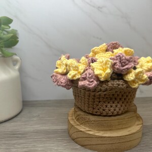 May include: A crocheted flower arrangement in a brown basket. The flowers are a mix of pink and yellow.