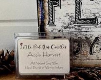 Puede incluir: Un pequeño recipiente de plástico transparente con una etiqueta blanca que dice "Little Red Hen Candles, Apple Harvest, All Natural Soy Wax, Hand Poured in a Warm Kitchen."