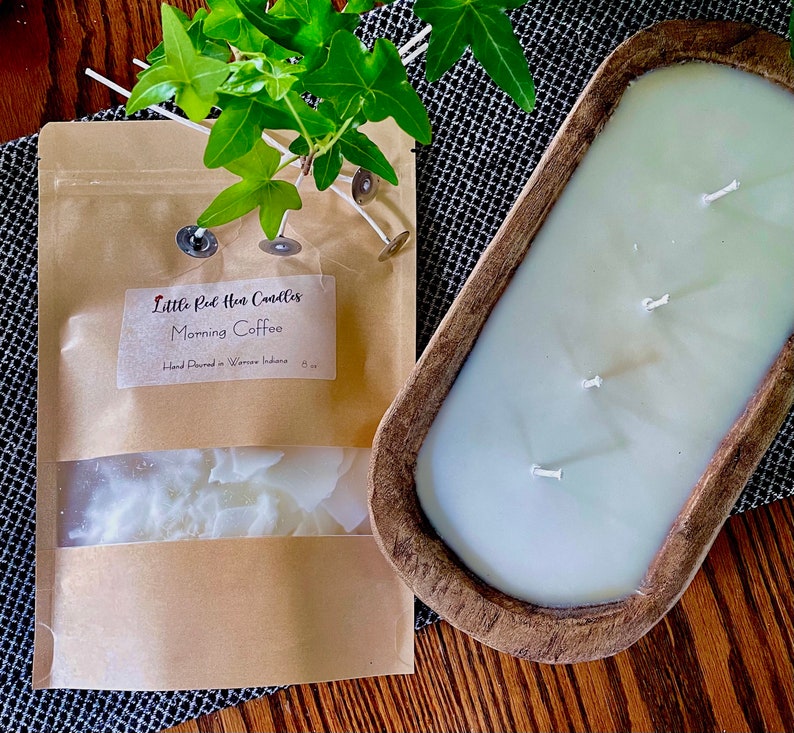 Op de afbeelding: Een bruine houten deegkomkaars met drie lonten. De kaars is wit en heeft een label met de tekst "Little Red Hen Candles Morning Coffee Hand Poured in Warren Indiana".