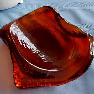 Peut inclure: Un bol décoratif en verre ambré de forme asymétrique unique. Le bol a une finition brillante et une teinte riche et chaleureuse. Les bords sont légèrement incurvés, ce qui ajoute à son attrait artistique. Idéal pour exposer de petits objets ou comme élément décoratif.