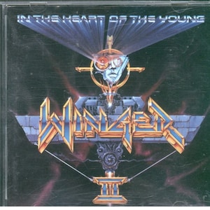 May include: A CD case with a black background and a futuristic design. The album cover features a silver robot head with red eyes and a gold and blue logo that says "WINGER" with the number "II" below it. The text "IN THE HEART OF THE YOUNG" is at the top of the image.