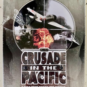 May include: A metal box with the title "CRUSADE IN THE PACIFIC" and the tagline "A WAR THAT SHOOK THE WORLD." The image inside shows a war scene with a plane and explosions. The box has a silver finish.