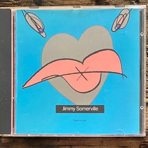 May include: A CD case with a blue background featuring a gray heart and a pink lip design with an X. The text "Jimmy Somerville" and "Read my Lips" are displayed. Two abstract shapes are at the top.