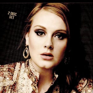 May include: DVD set featuring Adele with the text "ADELE" at the top. The cover includes a portrait of Adele with dramatic eye makeup and a patterned top. The title "THE STORY SO FAR" is displayed at the bottom, with "Documentary & Interview Collection" below.