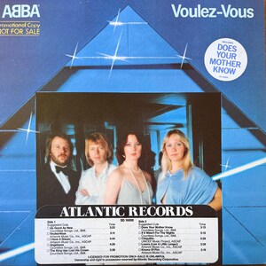 May include: ABBA's "Voulez-Vous" album cover. The album art features the band members in a group photo, with the album title at the top. The Atlantic Records logo is at the bottom, with a tracklist. The cover is predominantly blue.
