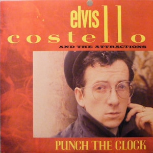 May include: A vintage record album cover featuring Elvis Costello and The Attractions. The cover is red with yellow text that reads "Elvis Costello and The Attractions" and "Punch The Clock". A photo of Elvis Costello wearing a black jacket and glasses is in the center of the cover.
