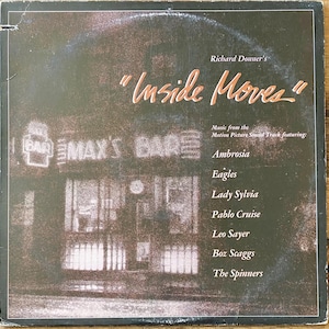 May include: Album cover for the "Inside Moves" soundtrack, featuring music from the motion picture. The cover is dark with the title in orange script. The names of the artists are listed below the title, including Ambrosia and Eagles.