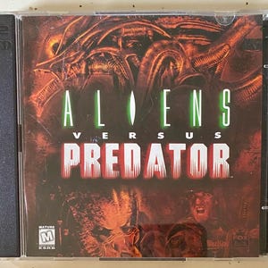 May include: A video game case for "Aliens Versus Predator." The cover features a dark, action-packed design with the game's title in green and red. The artwork depicts alien and predator imagery, with the ESRB rating visible.