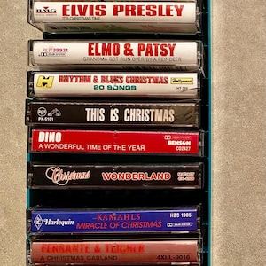 May include: A collection of Christmas music cassette tapes in a teal case. Titles include Mannheim Steamroller, Elvis Presley, and The Chipmunks. The tapes are in various colors, with text labels.