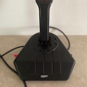 May include: Black Kraft joystick with a red button on the side and two red buttons on the top. The joystick has a black handle and a black base. The word "Kraft" is printed on the front of the base.