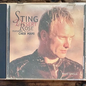 May include: CD case for Sting's single "Desert Rose" featuring Cheb Mami. The cover features a portrait of Sting with the title in a stylized font. The words "MAXI SINGLE" are printed on the bottom right.