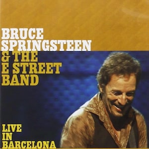 May include: A DVD case with a gold and blue background. The text reads "BRUCE SPRINGSTEEN & THE E STREET BAND LIVE IN BARCELONA." A smiling man is visible on the right side of the case.