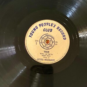May include: A vintage vinyl record with a cream-colored label featuring the text "Young People's Record Club." The label includes the title "Violin," the names of the writer, and the performer. The record is black with visible grooves.