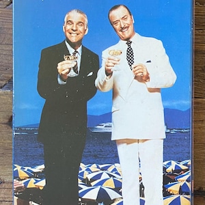 May include: A VHS tape for the movie "Dirty Rotten Scoundrels" featuring Steve Martin and Michael Caine. The cover has a blue background with the title in pink and two men in suits holding glasses. The Orion Home Video logo is at the bottom.