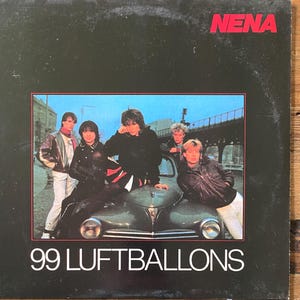 May include: A vintage vinyl record album cover featuring the band Nena. The album cover is black with the band's name in red at the top. The album title, "99 Luftballons," is in white at the bottom. The image shows the band members posing on and around a car.