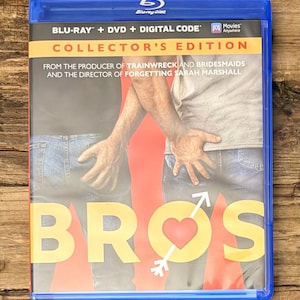 May include: A blue Blu-ray case featuring the movie "Bros." The cover art shows two people in jeans with hands on their backsides, with the word "BROS" in large yellow letters and a heart with an arrow. The case includes "Collector's Edition" text.