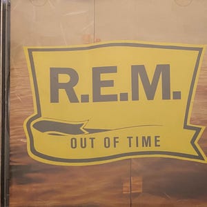 May include: A yellow and black CD case with the band name "R.E.M." and the album title "Out of Time" printed on the front.