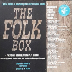 May include: A black and white album cover with the title "The Folk Box" in large, bold letters. The cover features a comprehensive anthology of American folk songs featuring artists such as Clarence Ashley, Theodore Bikel, Oscar Brand, Big Bill Broonzy, Hamilton Camp, Ian Campbell Folk Group, Judy Collins, and many others. The album includes 4 twelve-inch high fidelity long play records.