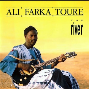May include: A man wearing a blue and white patterned robe plays a black electric guitar. The background is a yellow desert landscape. The album cover text reads "ALI FARKA TOURE THE river".