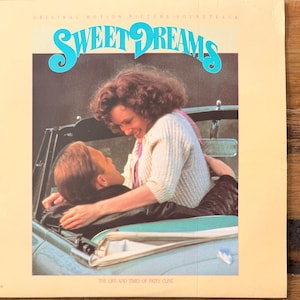 May include: Vintage vinyl record album cover for the "Sweet Dreams" soundtrack. The cover features a couple in a convertible car. The title is in turquoise script. The text "The Life and Times of Patsy Cline" is at the bottom.