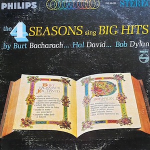 May include: A vintage vinyl record cover featuring the 4 Seasons singing big hits by Burt Bacharach, Hal David, and Bob Dylan. The cover features a stylized image of an open book with song titles listed on each page.