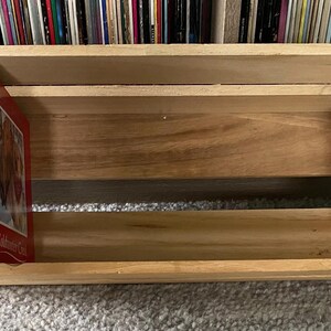 May include: A wooden CD storage crate with two shelves. The crate is empty except for a stack of CDs on the top shelf. The CDs are mostly green and red with white text. The text on the red CD reads "Christmas Classics, More Songs for the Holidays, Volume 1".