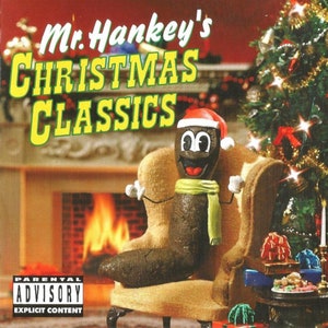 May include: Mr. Hankey, a brown cartoon character wearing a Santa hat and a green scarf, sits in a plush armchair in front of a fireplace. A Christmas tree with ornaments and lights is in the background. The text "Mr. Hankey's Christmas Classics" is displayed in large, colorful letters at the top of the image. A parental advisory label is in the bottom left corner.