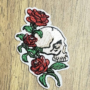 Könnte beinhalten: Gestickter Bügel-Patch mit einem weißen Totenkopf mit einer roten Rose und grünen Blättern.