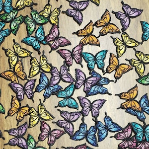 Puede incluir: Una colección de parches de mariposa de colores para planchar. Los parches son de varios tonos de azul, verde, morado, naranja y amarillo. Las mariposas son de diferentes tamaños y posiciones, creando un diseño vibrante y caprichoso.