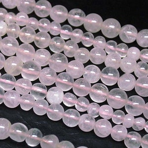 May include: A strand of pale pink rose quartz beads. The beads are round and smooth, with a translucent appearance. The beads are strung on a clear thread.