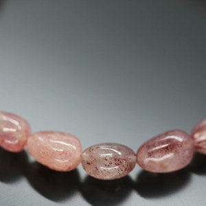 May include: Close-up of a pink and red gemstone bracelet with oval-shaped beads. The beads have a translucent appearance with subtle red inclusions.