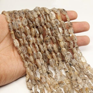 May include: A strand of translucent oval-shaped beads with brown and black flecks. The beads are strung on a clear thread.