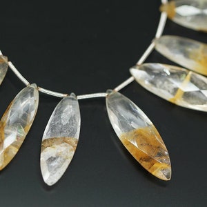 May include: A strand of faceted, clear quartz beads with brown inclusions. The beads are teardrop shaped and strung on a silver wire.