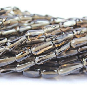May include: A strand of dark brown teardrop-shaped glass beads. The beads are translucent and have a slight shimmer.