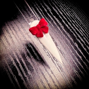 May include: A white nail with a red bow accent. The nail is long and pointed.