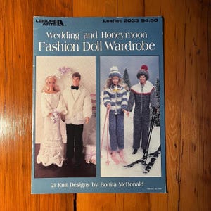 May include: A blue leaflet titled "Wedding and Honeymoon Fashion Doll Wardrobe" featuring images of knitted doll outfits. The cover includes text "21 Knit Designs by Bonita McDonald" and the Leisure Arts logo.