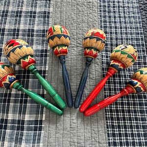May include: Six colorful maracas with green, blue, red, and yellow paint. The maracas are made of wood and have a rounded shape.