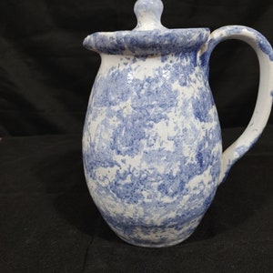 May include: A white ceramic pitcher with a blue and white marbled glaze. The pitcher has a lid and a handle.