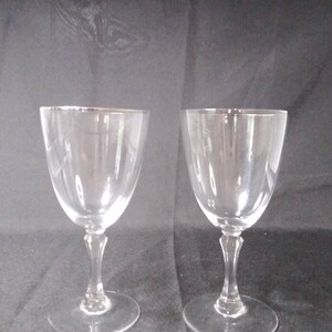 May include: Two clear glass wine glasses with a silver rim. The glasses have a tall, slender stem and a round bowl.