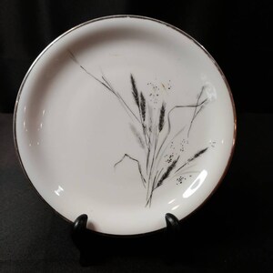 May include: White ceramic plate with a silver rim and a black and white floral design of grass and wheat.