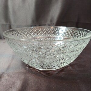 May include: A clear glass bowl with a diamond pattern. The bowl is empty and sitting on a brown surface.