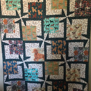 May include: A large, square quilt featuring a patchwork design with various dog breeds. The quilt showcases squares with different dog patterns in shades of brown, teal, and black, set against a white background with floral and paw print accents. The quilt is bordered in dark green.