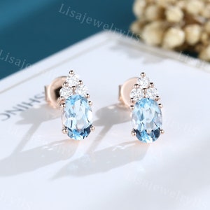 May include: A pair of earrings with a light blue oval gemstone surrounded by smaller clear gemstones. The earrings are set in rose gold.